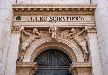 Fototapeta premium Fragment of the entrance door to the Lyceum, Venice, Italy. The old entrance is richly decorated with sculptures. Above the door are three figures of angels. The columns end with the capital