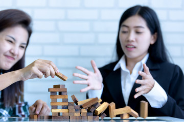 Fototapeta premium Teamwork and cooperation concept - business women building a structure of wooden blocks and wooden blocks structure falling on table surface . 
