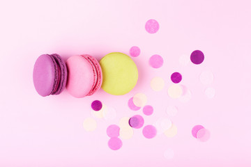 Three colorful macarons on pink background decorated with cinfetti. Top view.