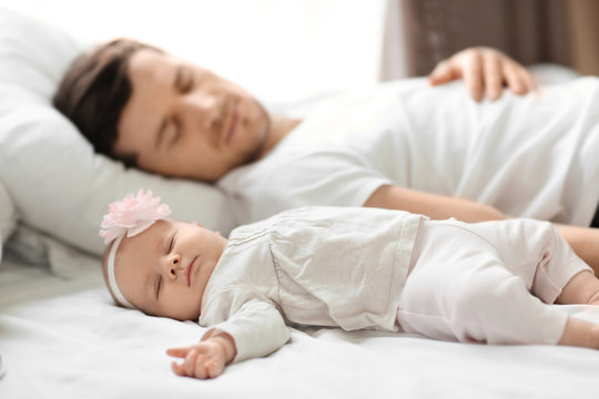 Young father with cute baby sleeping on bed at home