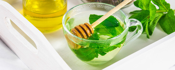 Mint tea in a cup, a jar of honey, a cookie in a jar, on a white tray in bed.