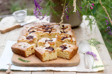 Pieces of fruit pie with pieces of plums and peach and a bouquet of flowers on a wooden table. Rustic style.