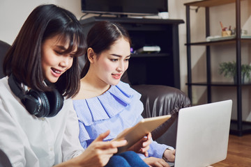 Asian girl in blue casual dress listening to music from black headphones and use laptop. In a comfortable and good mood, In the living room on the sofa.