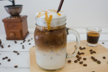 Ice caramel macchiato coffee on white wooden table background with coffee grinder and coffee bean.