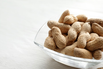Bowl with tasty peanuts on wooden table