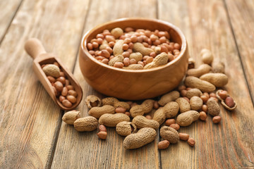 Bowl and scoop with tasty peanuts on wooden table