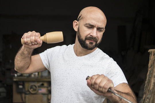 white bald carpenter with beard in white t-shirt works as a chisel and a mallet