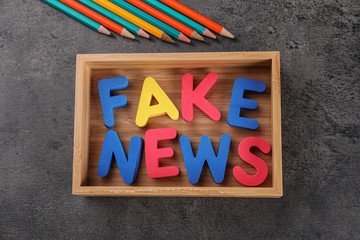 Phrase FAKE NEWS made with color letters in wooden box on gray background