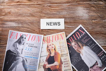 Paper with word NEWS and fashion magazines on wooden background