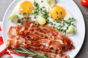 Plate with tasty bacon and fried eggs on table