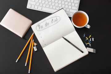 Empty to-do list, computer keyboard and cup of tea on dark background