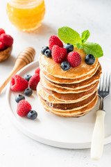 Pancakes with berries, honey and mint on white plate, closeup view, selective focus. Stack of pancakes. Tasty dessert or breakfast