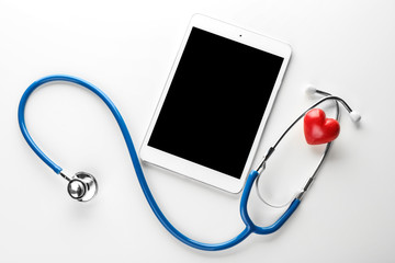 Stethoscope with small heart and tablet PC on white background