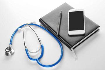 Stethoscope with smartphone and notebook on white background