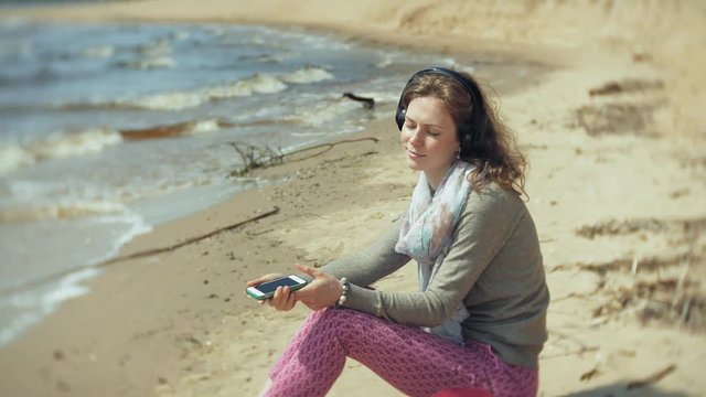 A woman listens to music on headphones, relaxes and dances on the shore of the sea river of the ocean. Technology in the open air