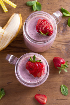 Two glasses of pink strawberry milkshake or cocktail. Strawberry banana smoothie on wooden table. overhead, vertical