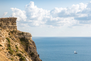 Fototapeta na wymiar the rocky shore. high rocky cliff and sailboat at sea. Fiolent, Crimea