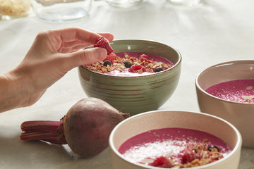 Two plates with smoothies on a white table, a woman's hand holds a raspberry