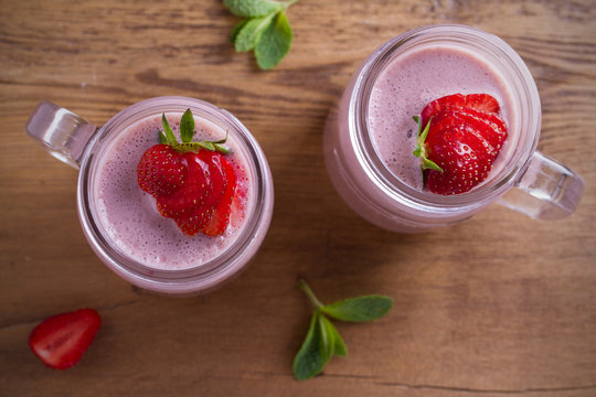 Two glasses of pink strawberry milkshake or cocktail. Strawberry banana smoothie on wooden table. overhead, horizontal