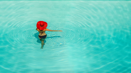 Beautiful girl in a swimsuit and a red hat in a blue water pool