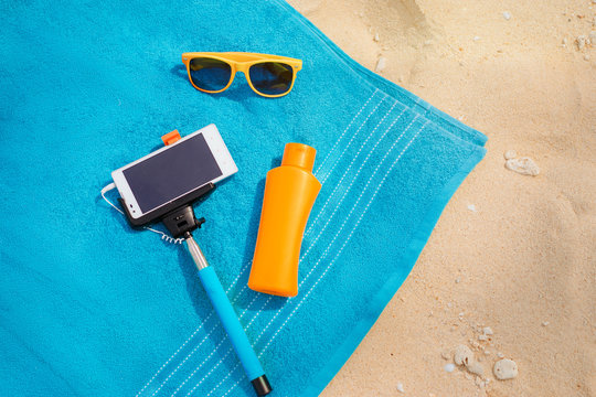 Vacation, Technology And Protection. Must Have Accessories On The Sea Beach. Smartphone, Selfie Stick, Sunscreen And Sunglasses. Top View.