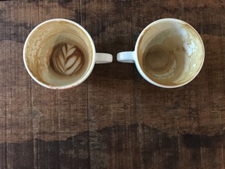 finished two cups of hot cappuccino and hot latte coffee with leftover latte art, put on natural dark brown wooden board table in cafe