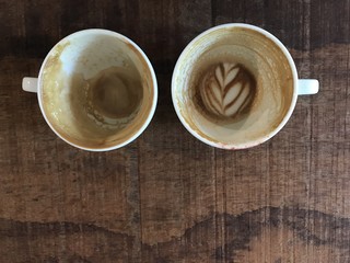 two cups of finished hot latte coffee with leftover latte art, put on natural dark brown wooden board table in coffee shop