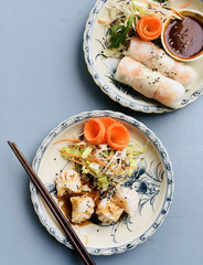 Asian style dinner. Flat-lay of steamed dumplings Dim sum and summer rice paper rolls with shrimp and sauce over blue table, top view, copy space. Chinese and vietnameese cuisine