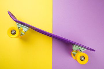 purple skateboard with yellow wheels on yellow and violet background. plastic mini cruiser board. minimalism, flat lay, copy space