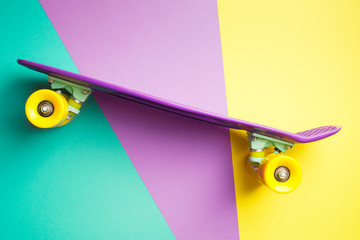 violet skateboard with yellow wheels on turquoise yellow and purple background. plastic mini...