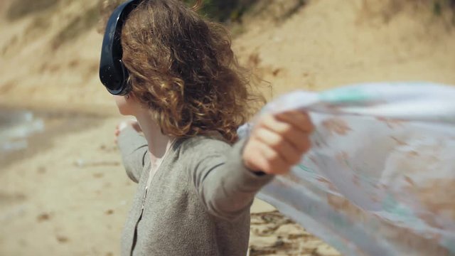 A woman listens to music on headphones, relaxes and dances on the shore of the sea river of the ocean. Technology in the open air