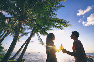 Romantic holidays. Youth and vacation. Young loving couple drinking beer together while resting on the sea beach enjoying sunset.