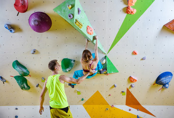 Young woman climbing bouldering problem (route), male instructor securing her