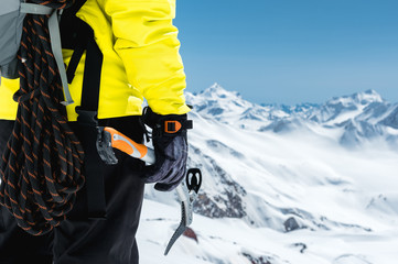 A mountaineer man holds an ice ax high in the mountains covered with snow. Close-up from behind. outdoor extreme outdoor climbing sports using mountaineering equipment