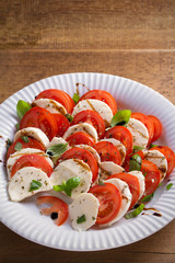 Caprese salad with tomatoes, mozzarella cheese, basil, olive oil and balsamic vinegar on white plate. vertical