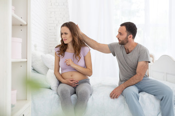 Obraz premium Dont worry. Appealing man and pregnant woman sitting on bed and man touching her head