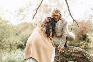 A beautiful couple in the boo style embraces sitting on a branch over the lake