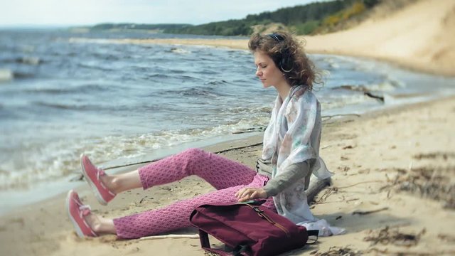 A woman listens to music on headphones, relaxes and dances on the shore of the sea river of the ocean. Technology in the open air