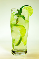 summer cold drink mojito lime and mint with ice and soda with drops on a glass on a white background