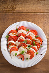 Caprese salad with tomatoes, mozzarella cheese, basil, olive oil and balsamic vinegar on white plate. overhead, vertical