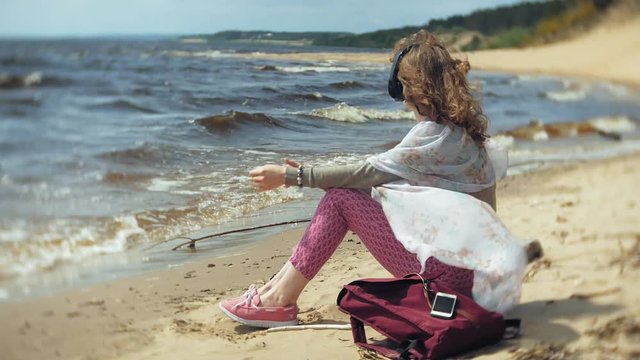 A woman listens to music on headphones, relaxes and dances on the shore of the sea river of the ocean. Technology in the open air