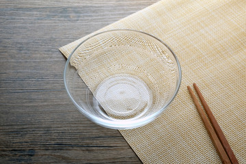 Glass bowl and chopsticks on wooden table.