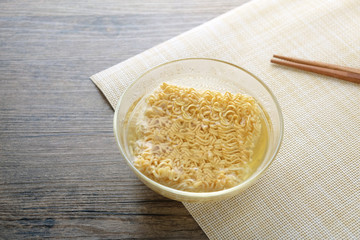 Glass bowl , chopsticks and instant noodle on the wooden table.