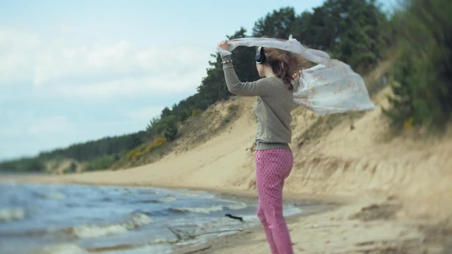 A woman listens to music on headphones, relaxes and dances on the shore of the sea river of the ocean. Technology in the open air