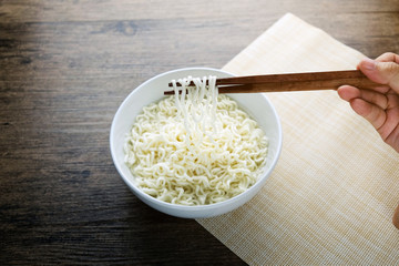 Top view of instant noodle in the glass bowl near the chopsticks on the wooden table.