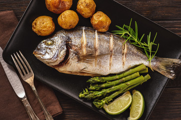 Baked dorado fish with potatoes, asparagus and tomatoes.