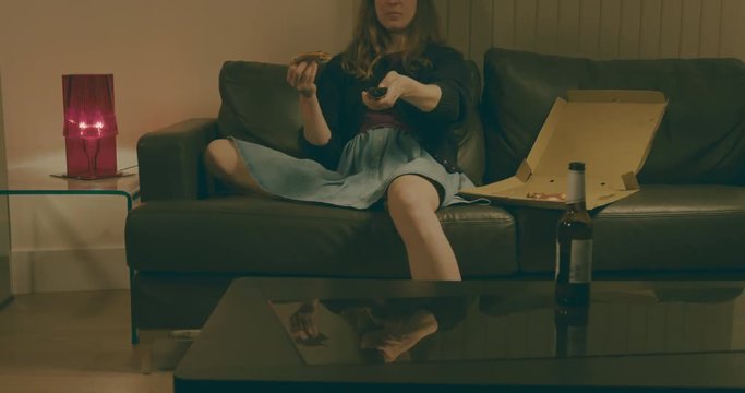 Young woman eating pizza and drinking beer at home by television