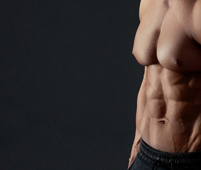 Muscular torso of male bodybuilder. Clear muscles relief on black stusio background. Sport...