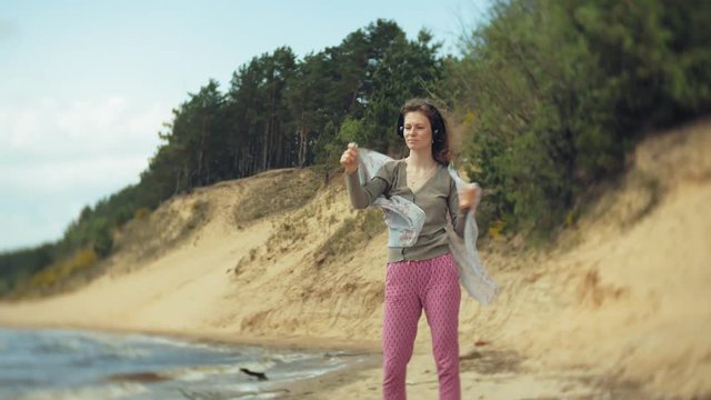 A woman listens to music on headphones, relaxes and dances on the shore of the sea river of the ocean. Technology in the open air
