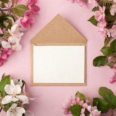 Festive flower apple tree composition and invitation on craft envelope on the pastel pink background. Overhead view